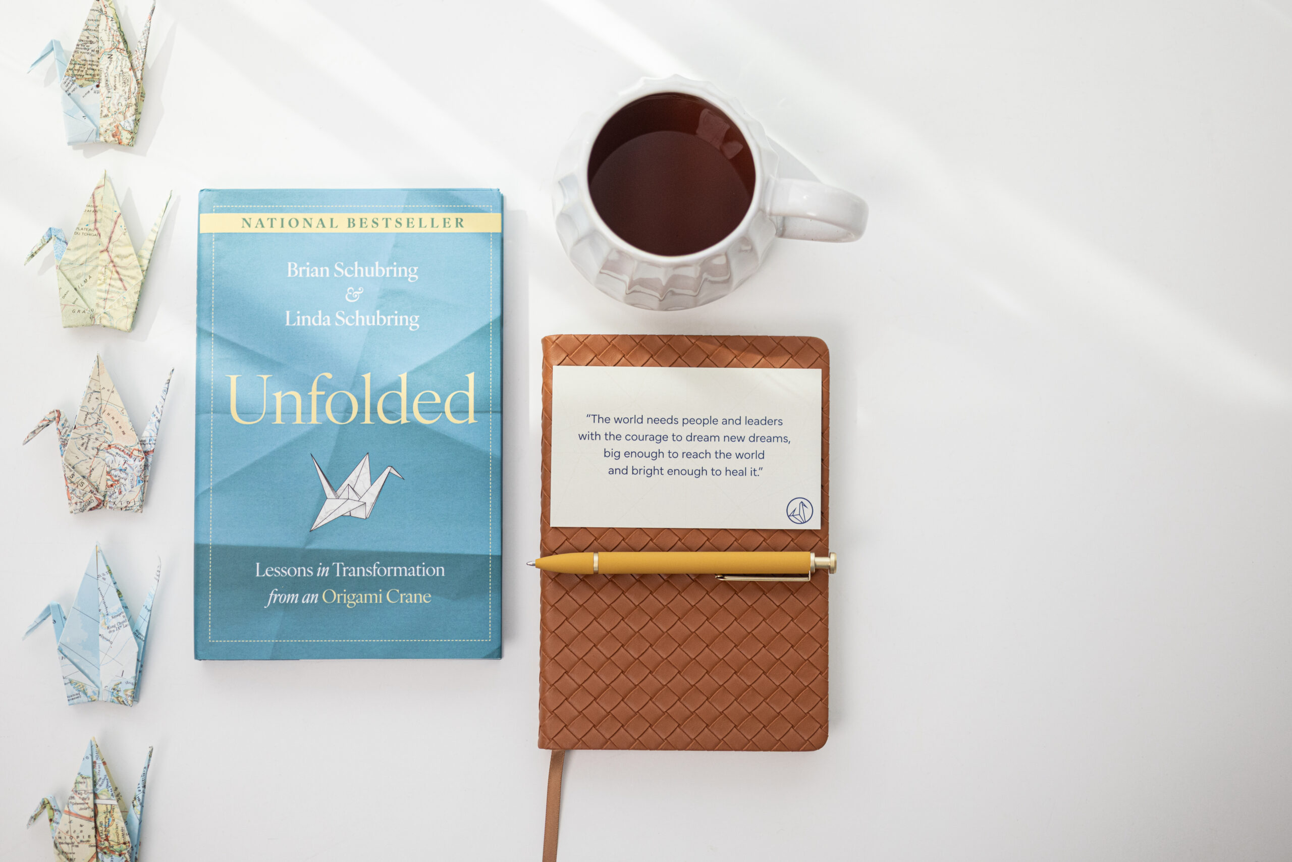 Unfolded book beside origami cranes, tea, and a journal with a quote about leadership